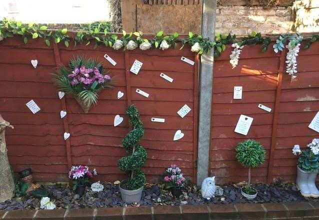 The fence in the back yard is decorated with a selection of ‘long-lasting’ flowers and shrubs as well as a full selection of tags displaying pithy sayings
